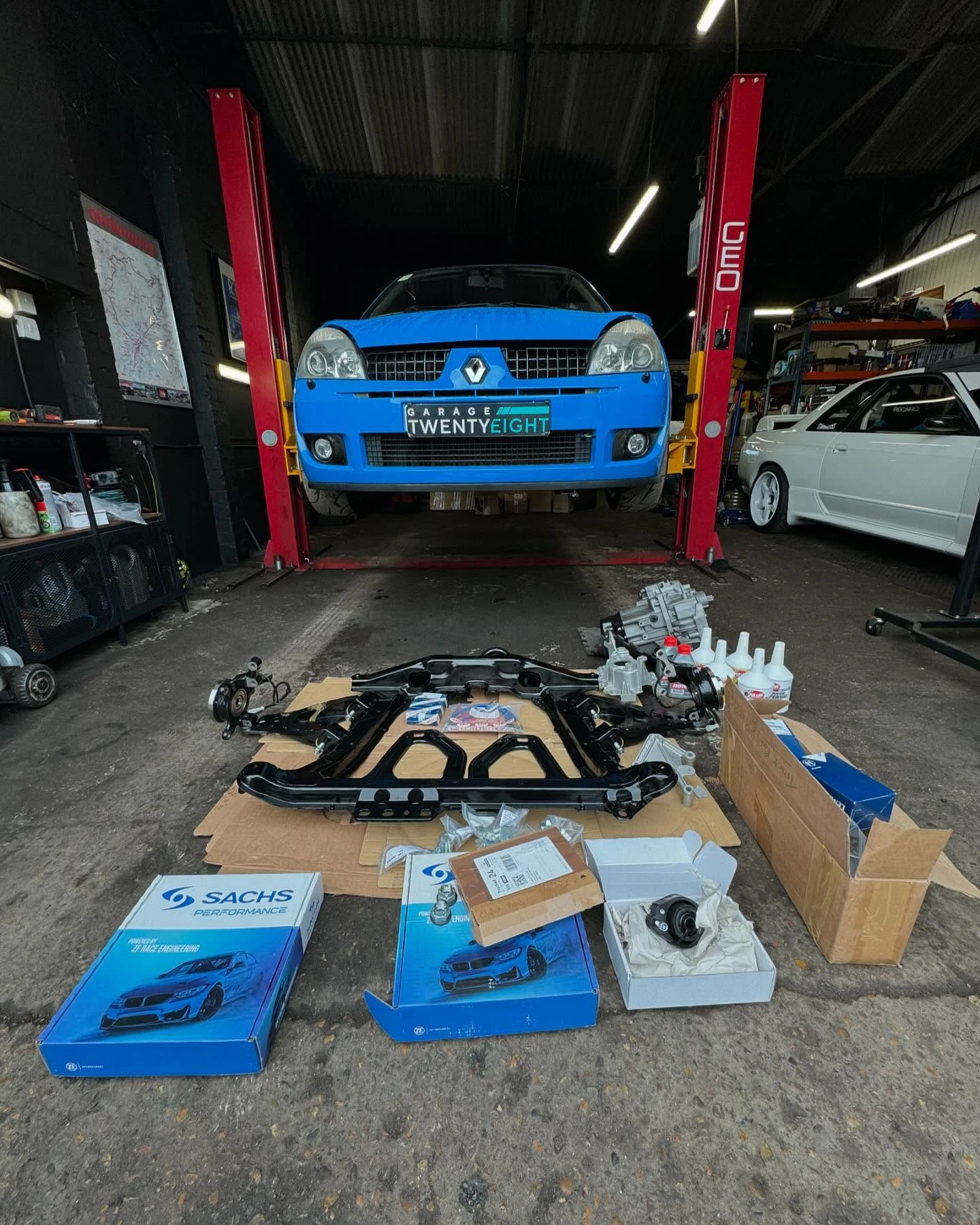 Blue Renault car on lift in garage with various car parts and boxes on the floor.