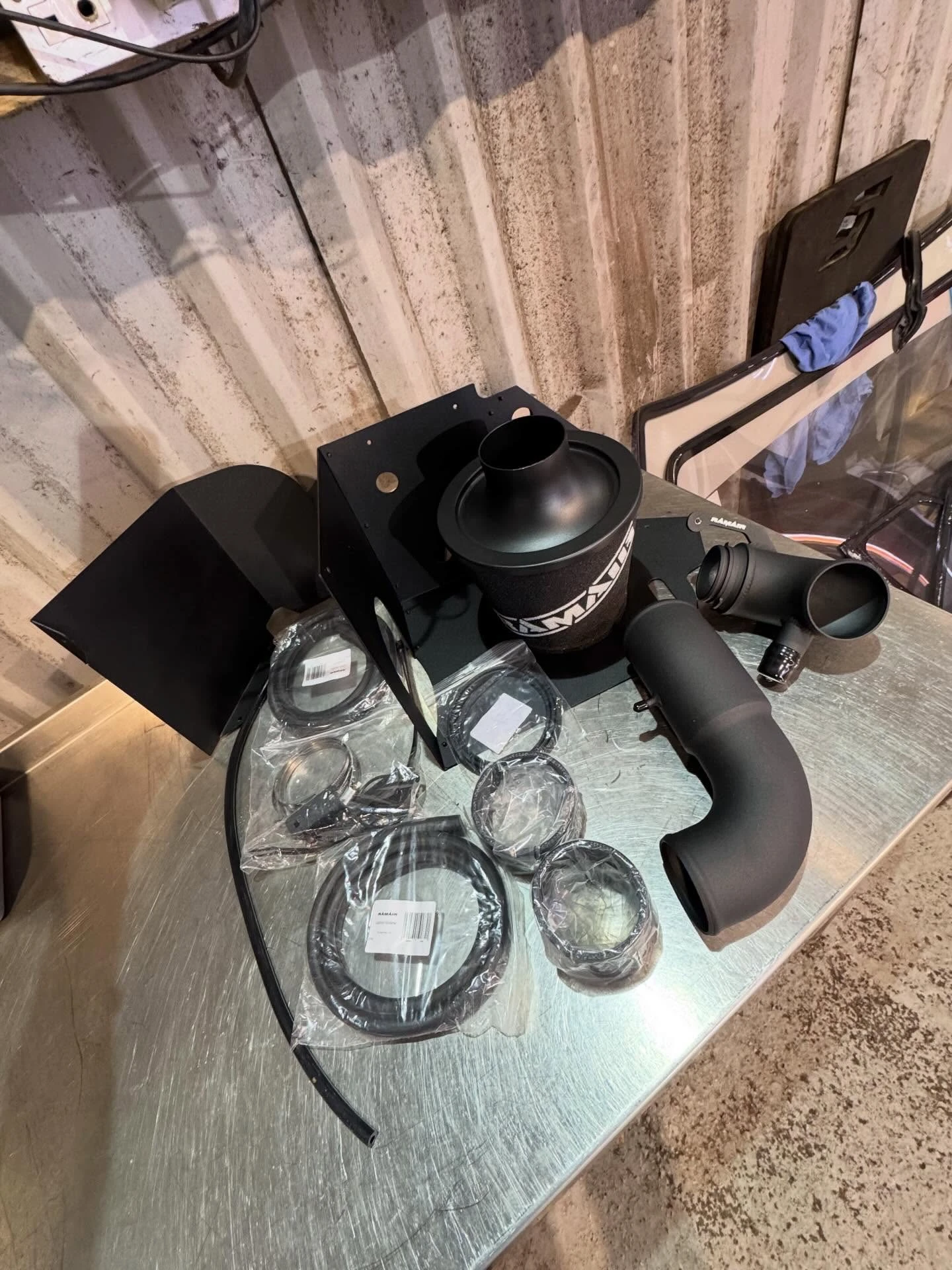 Disassembled black automotive air intake system with tubes, clamps, and filter on a metal surface.
