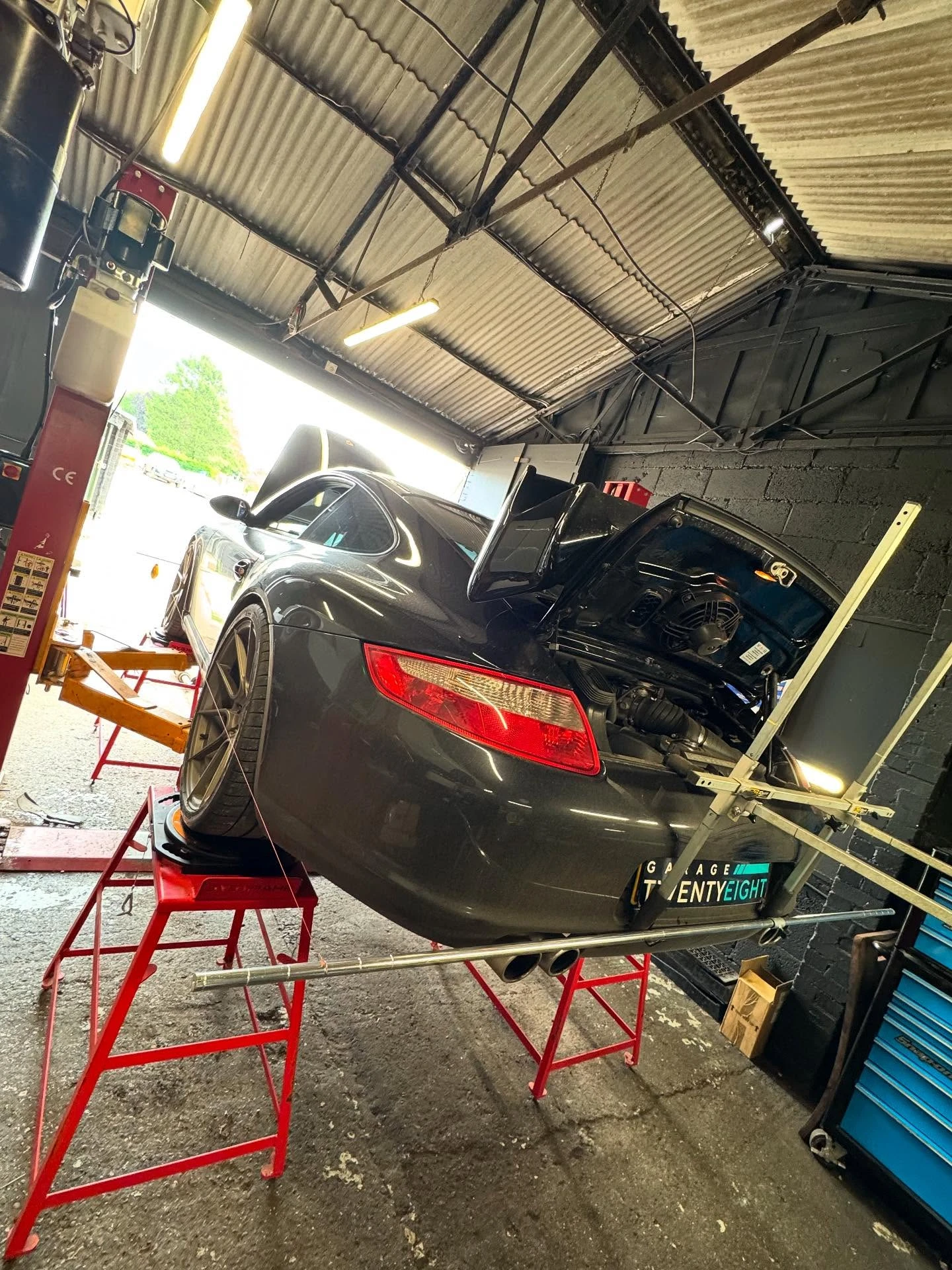 Gray sports car raised on red stands in garage with rear hood open for engine work.