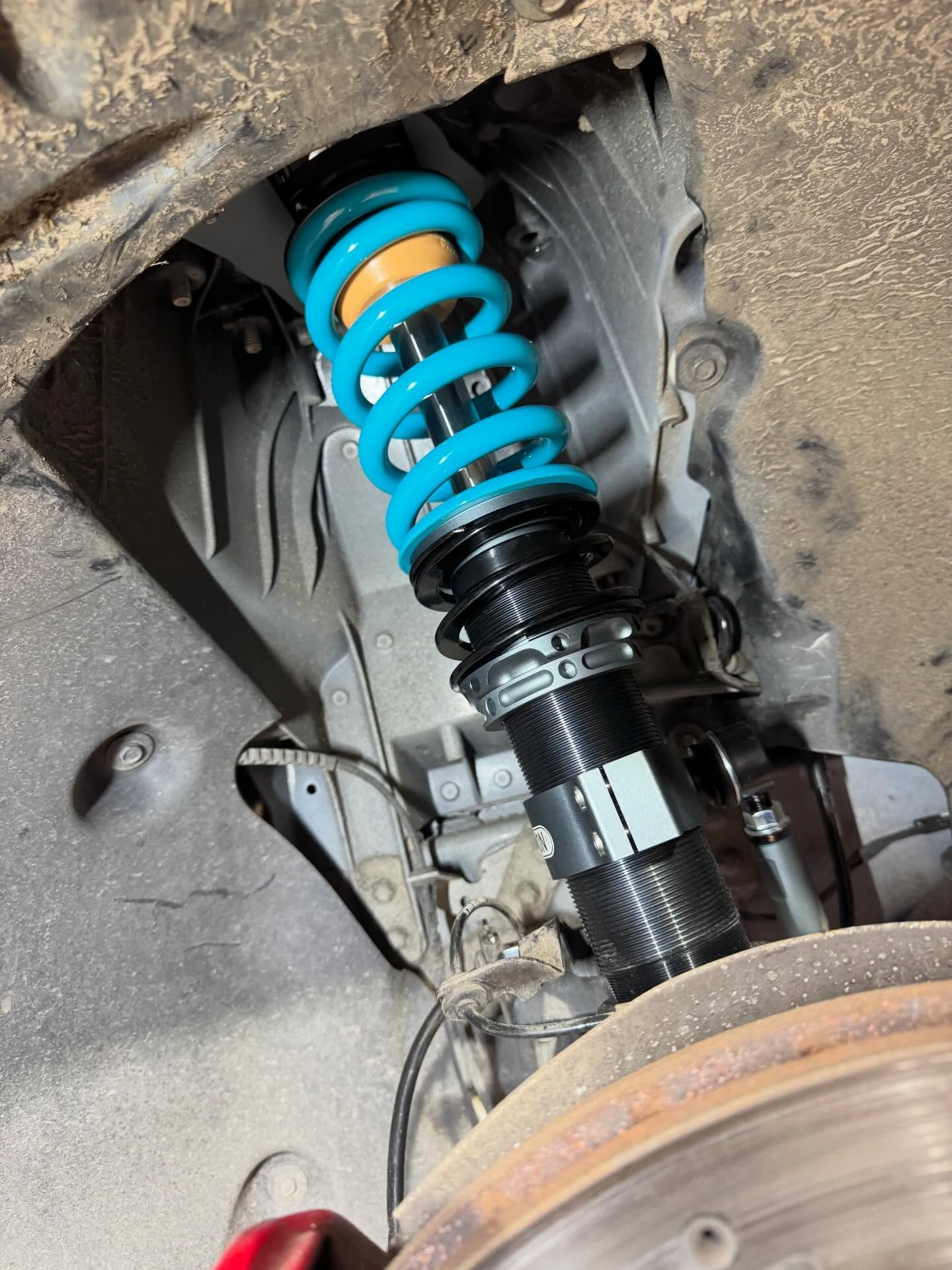 Close-up of a car suspension coilover with a blue spring and brake rotor in the wheel well.