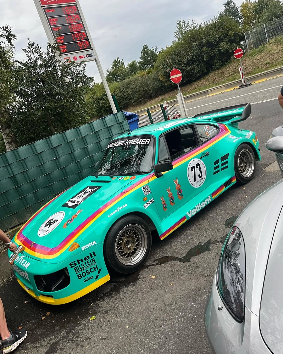 Turquoise Porsche race car with number 73 and Vaillant branding parked near a gas station sign.