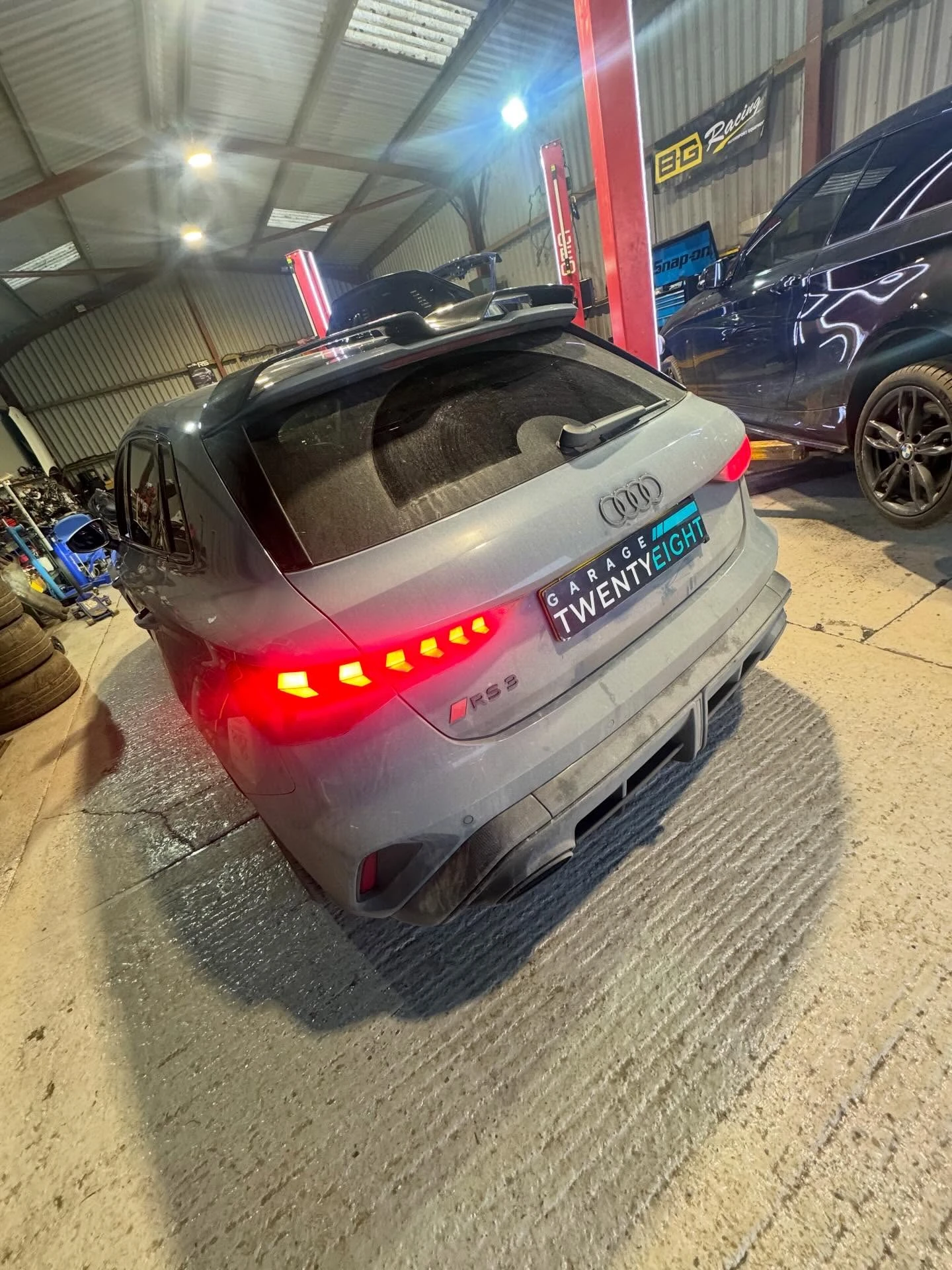 Rear view of a gray Audi RS Q3 with red taillights illuminated inside a garage.