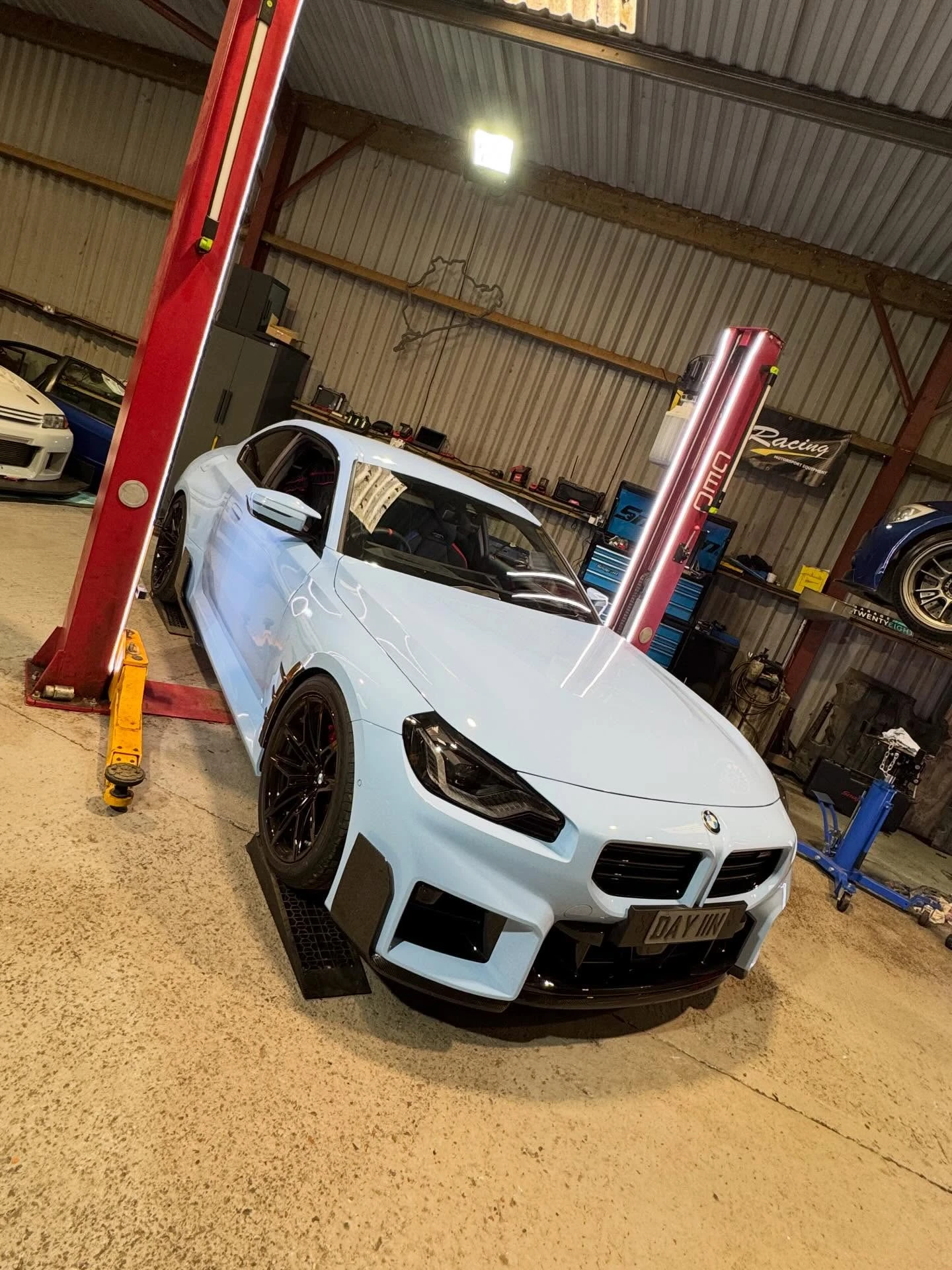 Light blue BMW car with black wheels parked indoors near red car lift pillars.