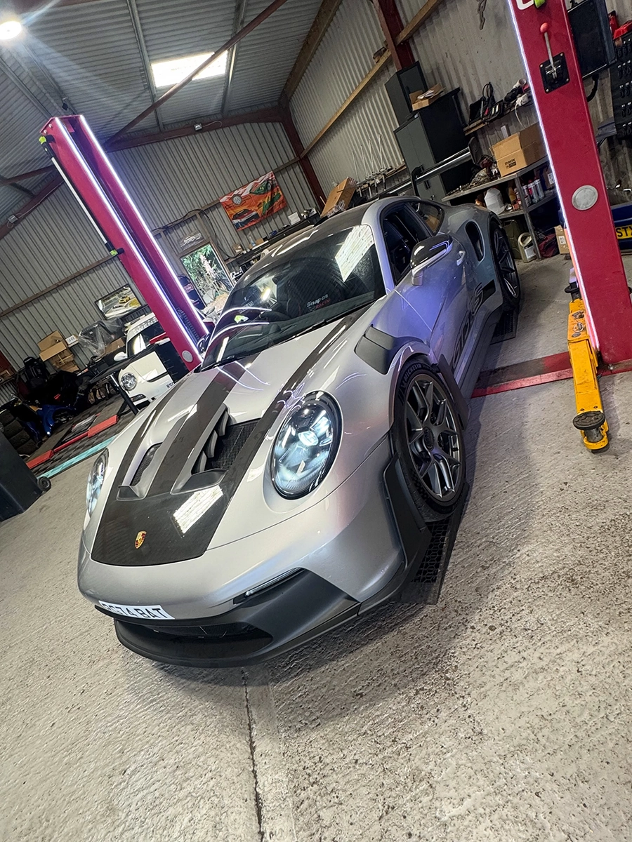 Silver Porsche sports car with carbon hood details parked inside a garage with red support beams.