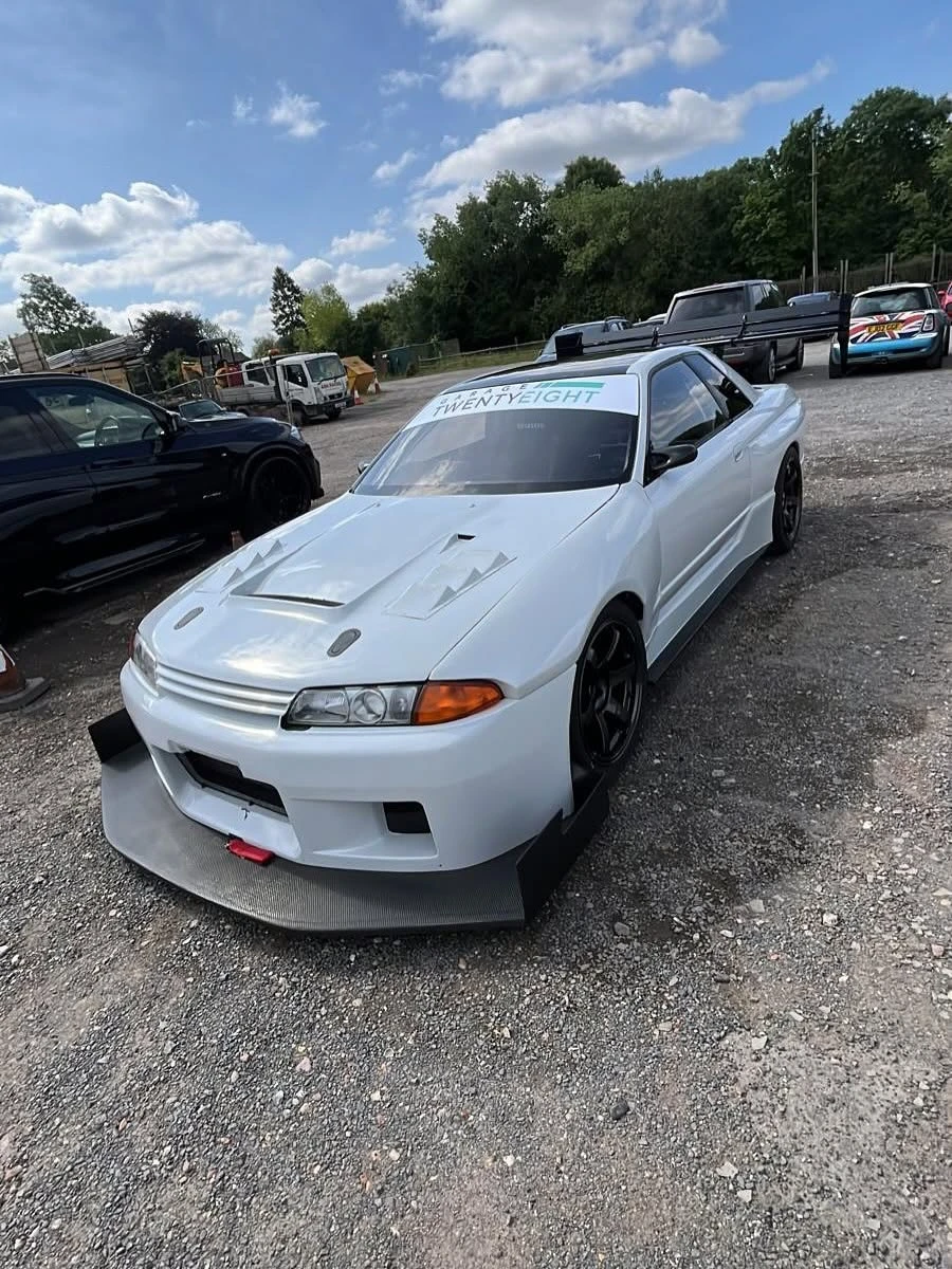 White race car with large front splitter and rear spoiler parked on gravel under blue sky.